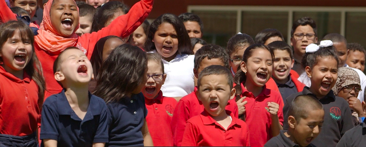 A large group of children are standing in a line with their arms in the air.