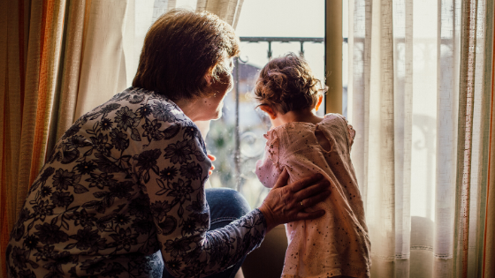 An elderly woman and a little girl are looking out of a window.