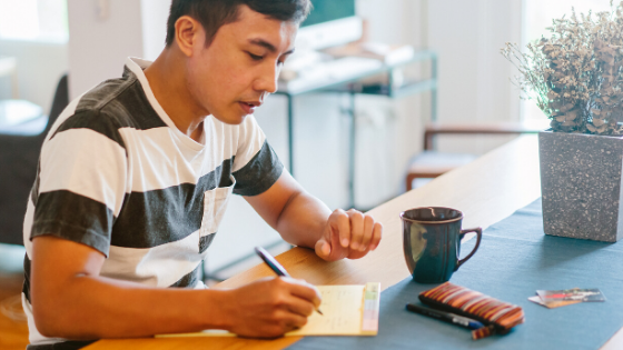 A man is sitting at a table writing on a piece of paper.