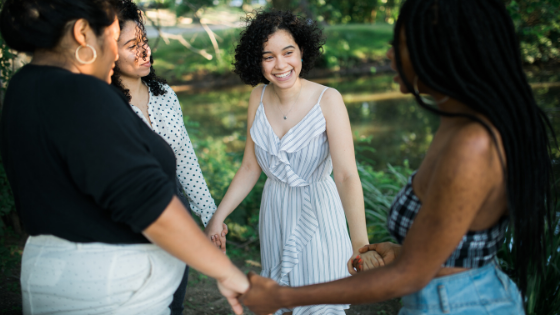 A group of women are holding hands in a circle in a park.