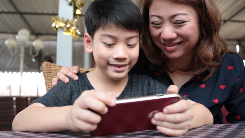 A woman and a boy are sitting at a table looking at a cell phone.