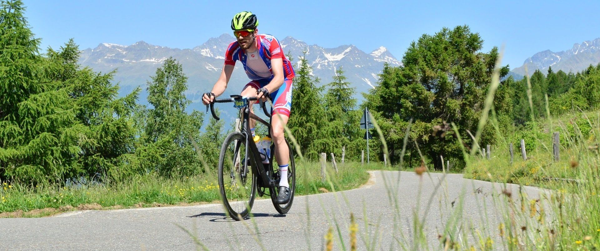 Ein Mann fährt mit dem Fahrrad eine Straße entlang. Im Hintergrund sind Berge zu sehen.