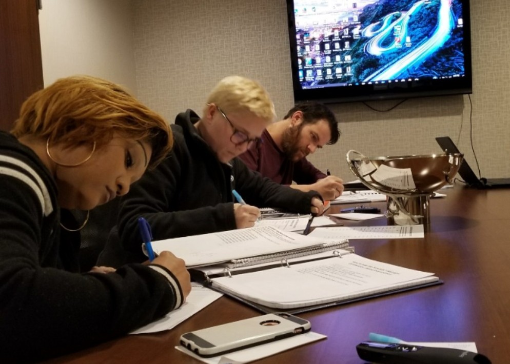 A group of people are sitting at a table writing on papers.