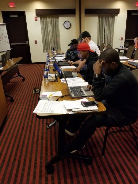 A group of people are sitting at tables with laptops