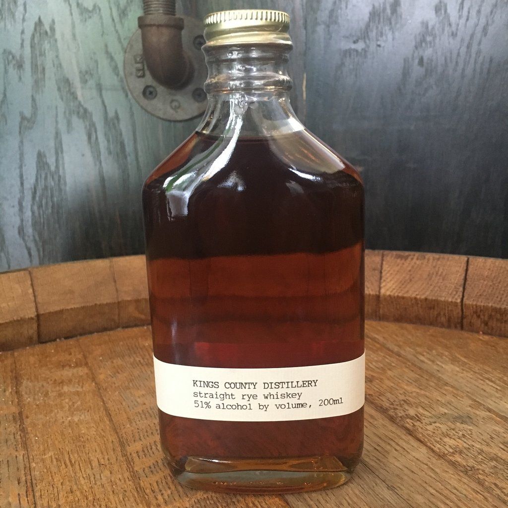 A glass bottle of dark amber liquid sits on a wooden surface; a label reads 