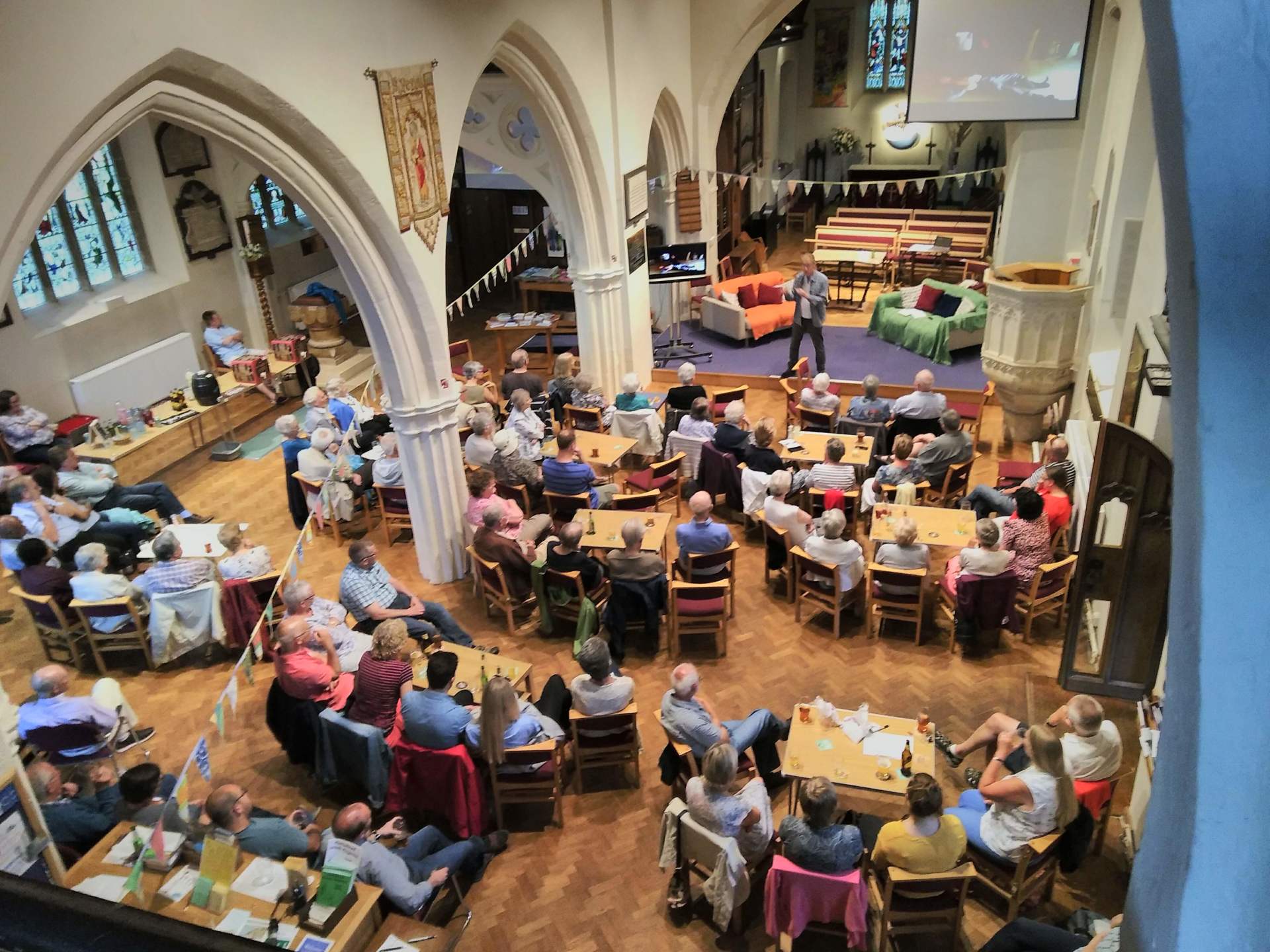 Large event in a church. People sit at tables, listening to a speaker on a stage.
