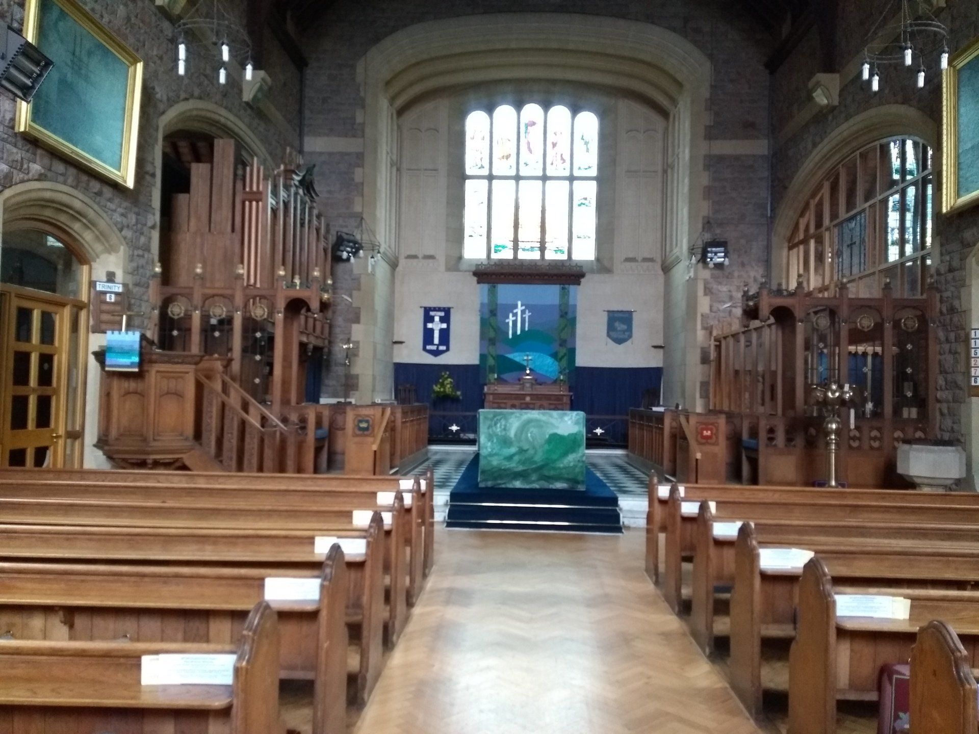 Interior view of a church with wooden pews, altar, and stained-glass window.