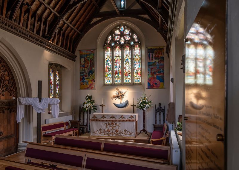Interior of a church with stained glass windows, wooden pews, and an altar. Sunlight streams through the windows.