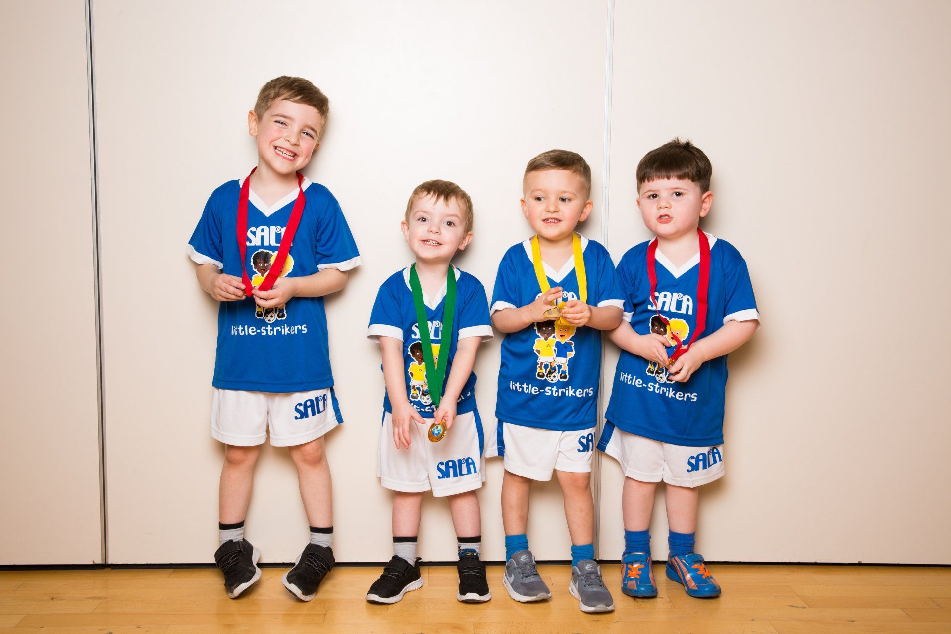 Four young boys wearing blue jerseys and medals posing indoors.