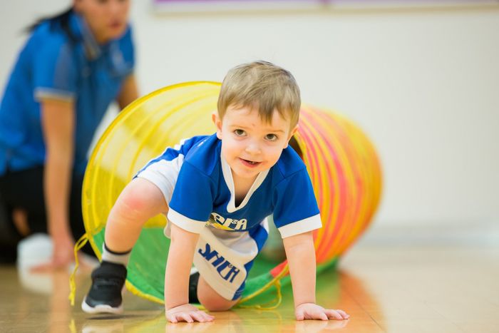 Young boy crawls through a colorful tunnel during gym class.