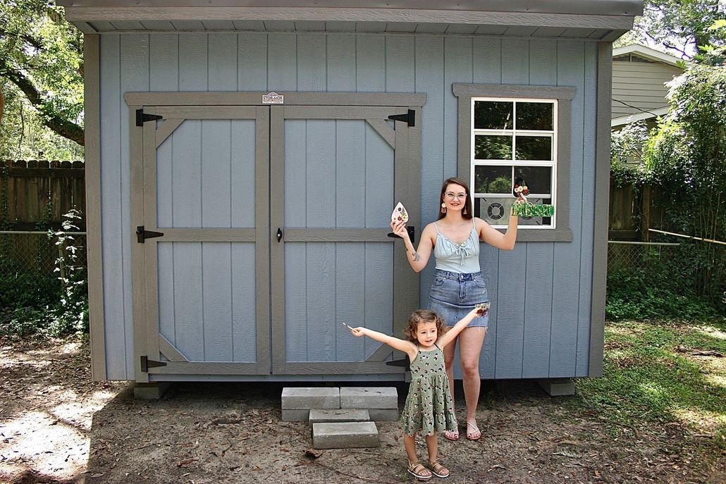 A woman and her little girl are standing in front of a blue shed they just bought.