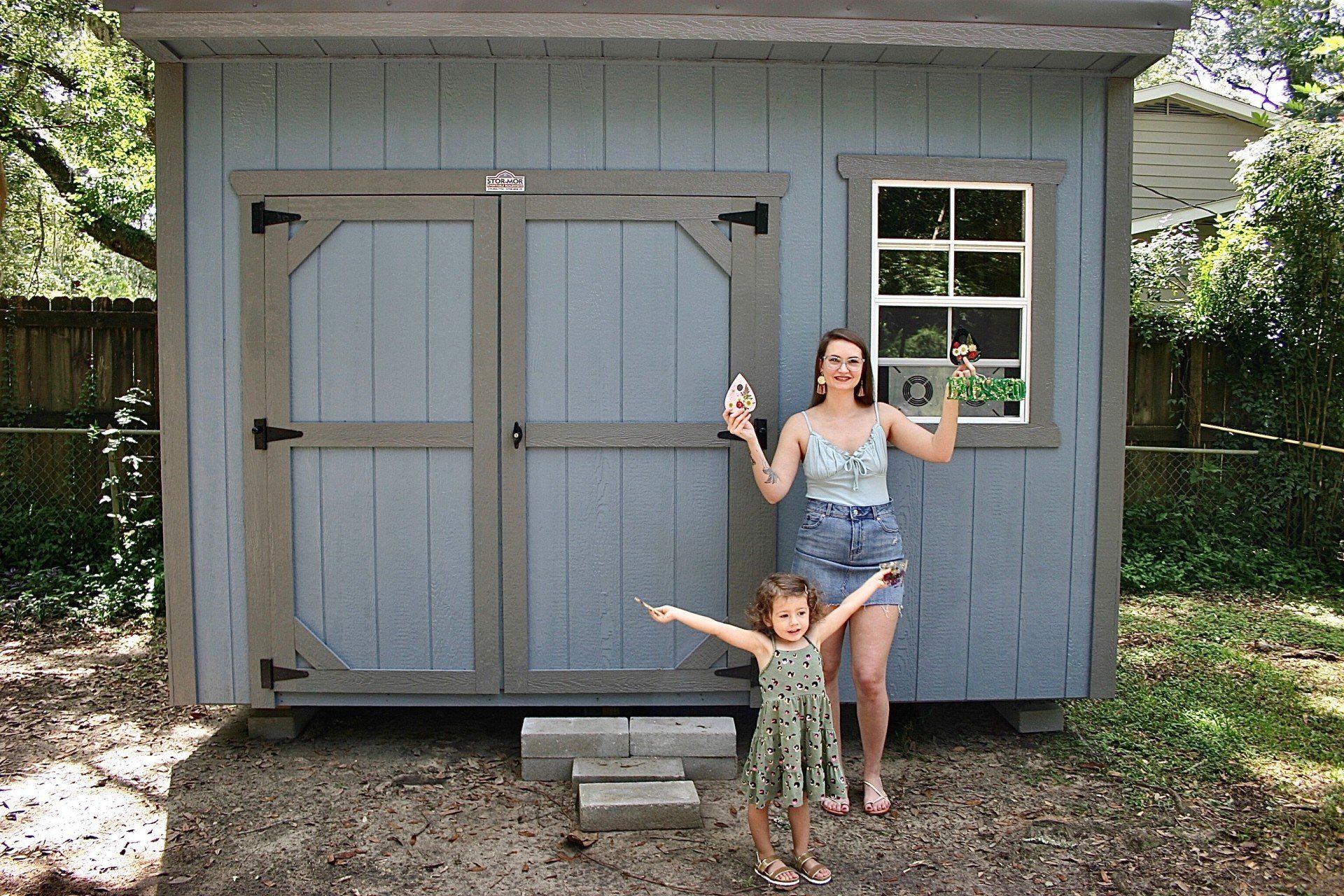 A woman and her little girl are standing in front of a blue shed they just bought.