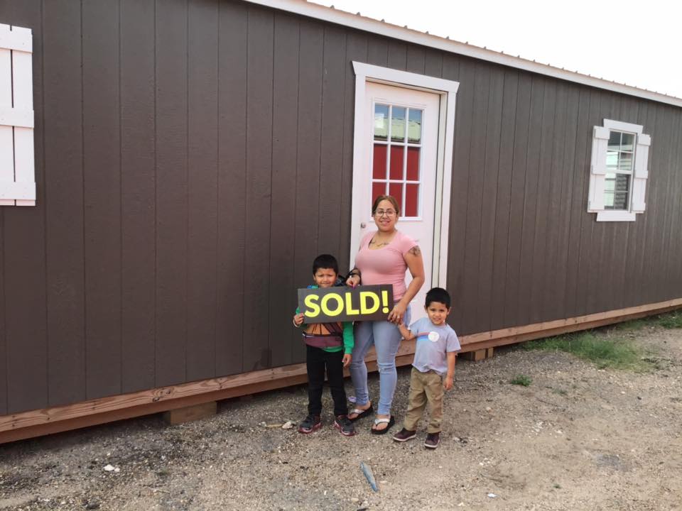 A woman and two children are holding a sold sign in front of a house.