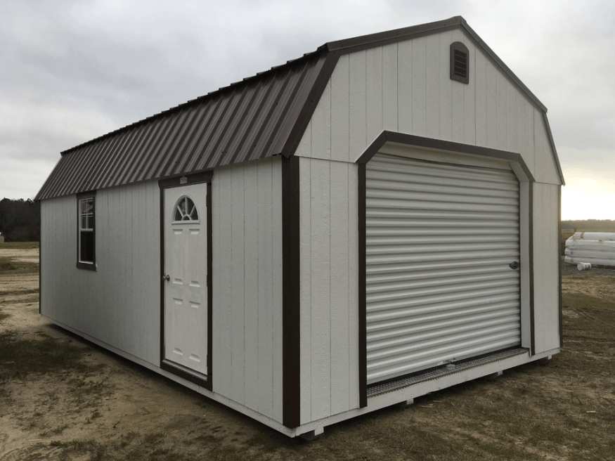 A white barn with a brown roof and a garage door.
