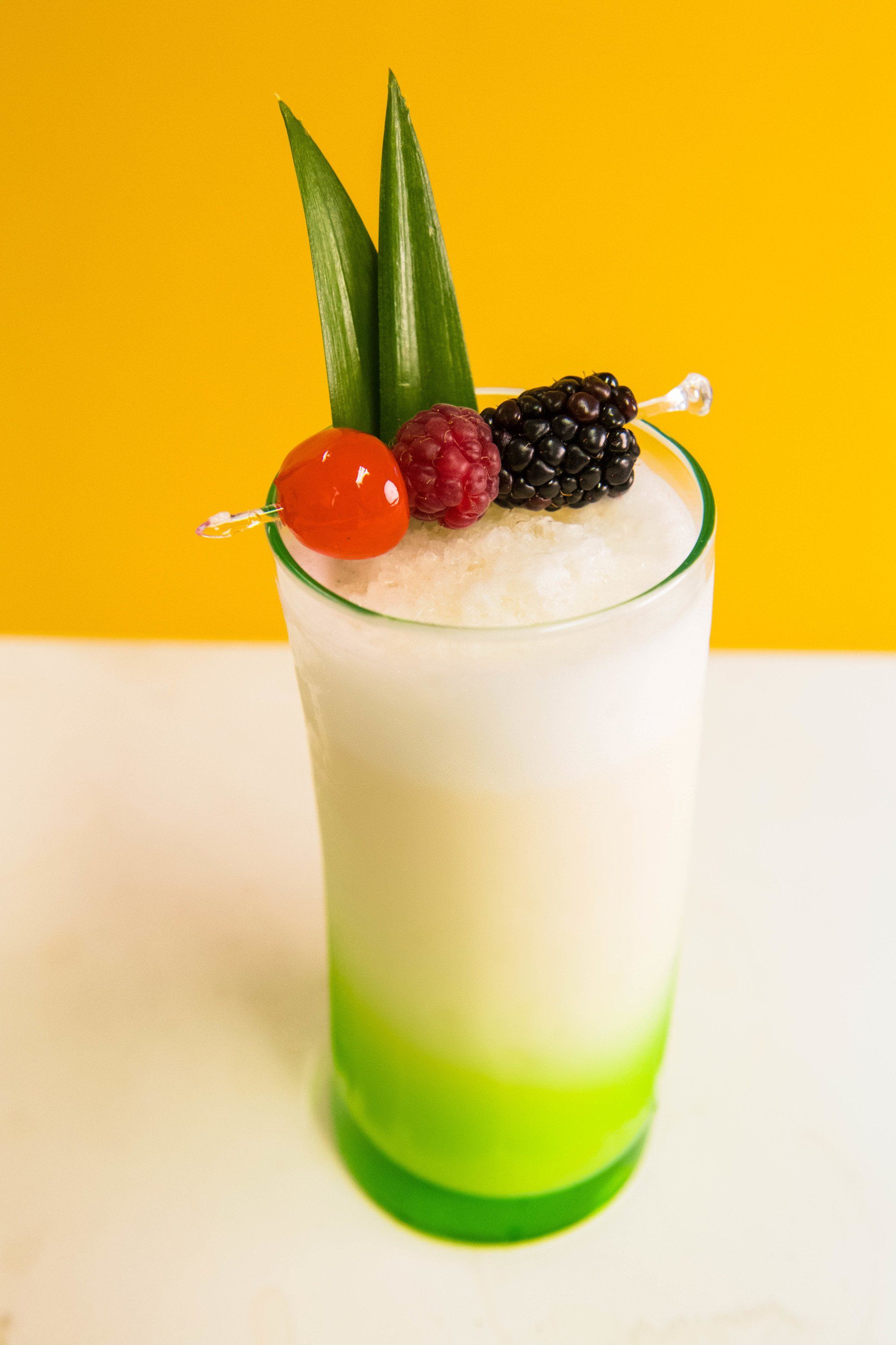 A green glass filled with a white liquid and berries on a yellow background.