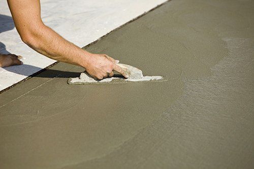 Person smoothing wet concrete with a trowel on a light gray surface.