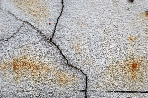 Cracked, weathered white surface with rust-colored stains, and dark cracks.
