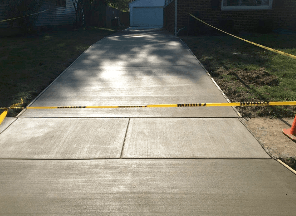 New concrete driveway, light gray, with caution tape. House and garage in background.