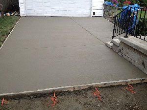 Freshly poured concrete driveway in front of a white garage. Black railing and brick edging are visible.