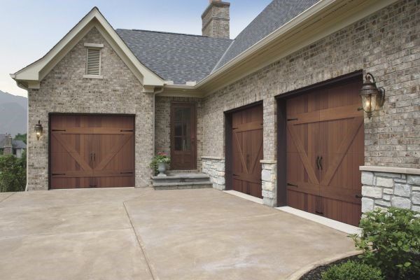 Three-car garage with wooden doors and brick exterior. Concrete driveway leads to the house, with mountain in the background.