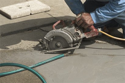A person using a circular saw to cut concrete, with a water hose nearby.