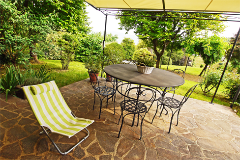 Patio with table and chairs, striped lounge chair, surrounded by greenery.