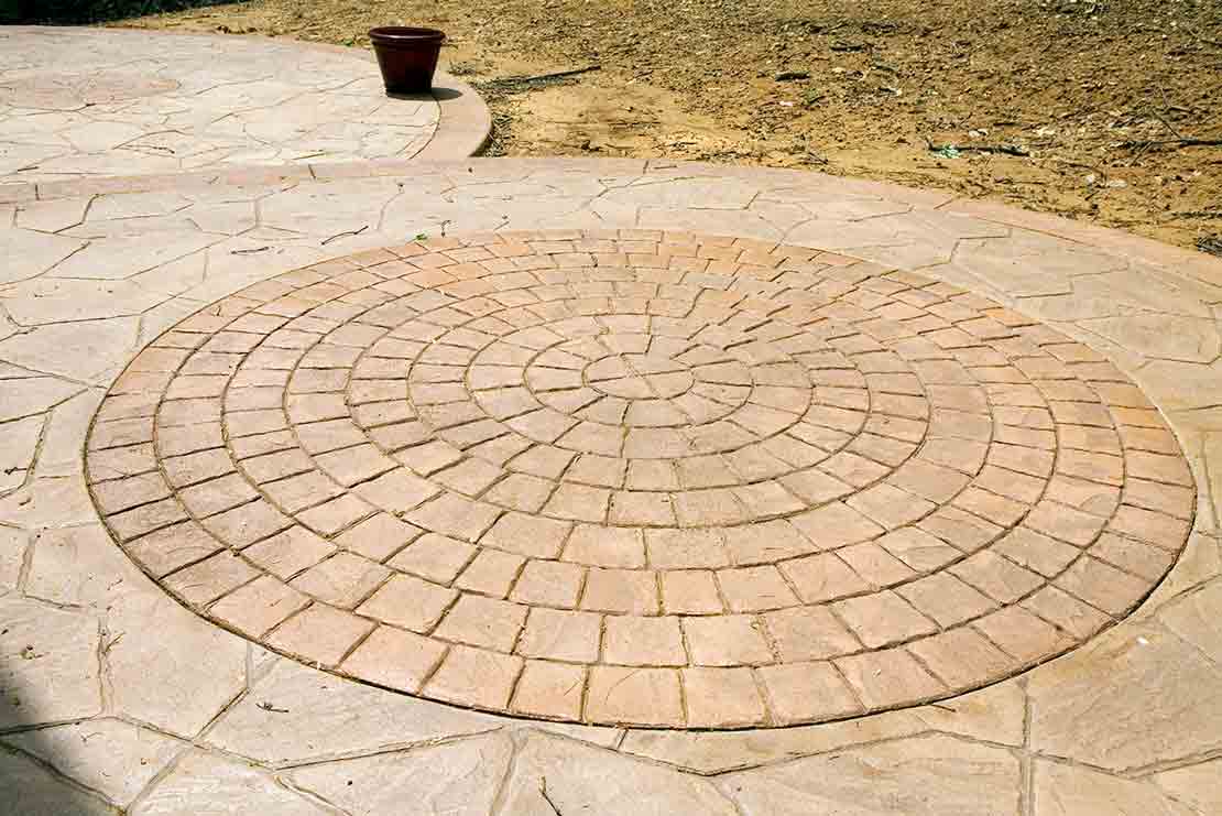 Circular brick pattern inset in concrete patio, brown pot in the background.