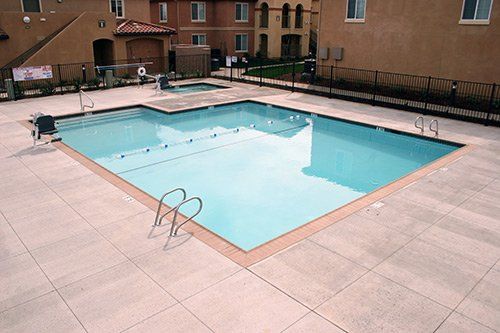 Swimming pool surrounded by light-colored tile, with buildings in the background.