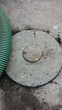 Circular concrete cover with raised center, green hose alongside, set in concrete.