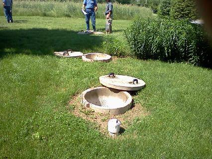 Concrete septic tank access points in a grassy yard, with two people standing nearby.
