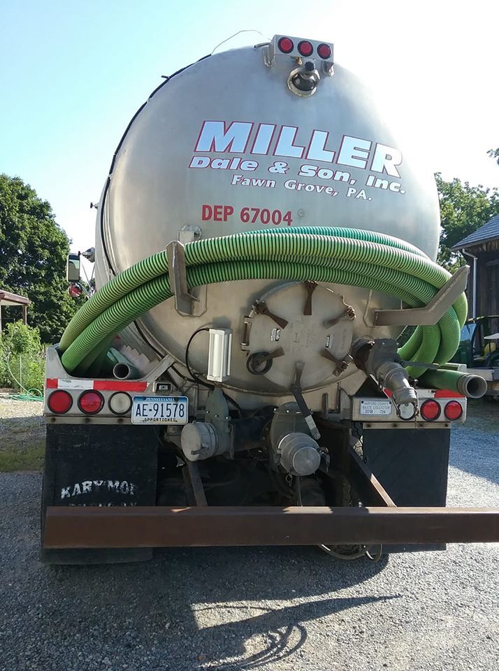 Rear view of a silver Miller waste transport truck with green hose, parked outdoors.