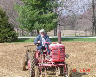 Man driving a red tractor in a field, smiling.