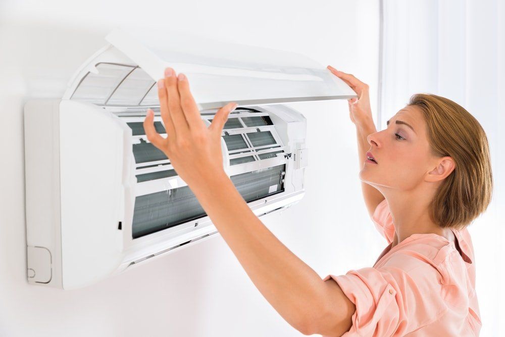 A picture of a female looking inside of a heat pump/air conditioning indoor unit