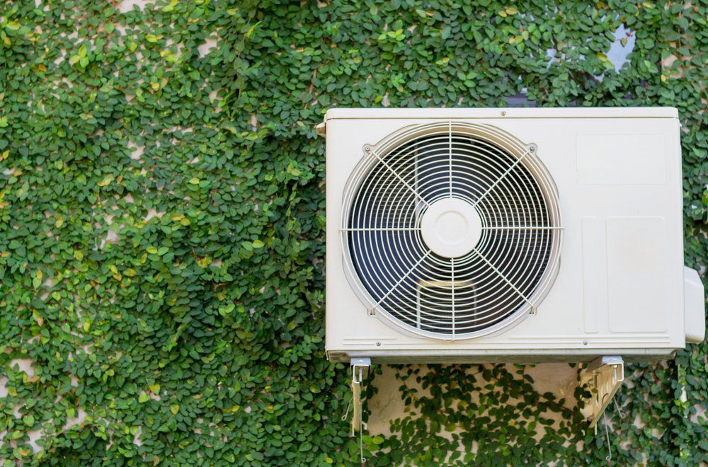 Heat pump outdoor unit on property covered in green leaves.