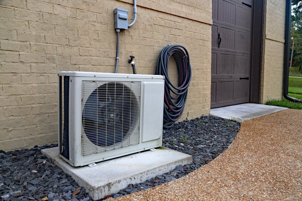 Outdoor heat pump unit on slab in front of brick property.