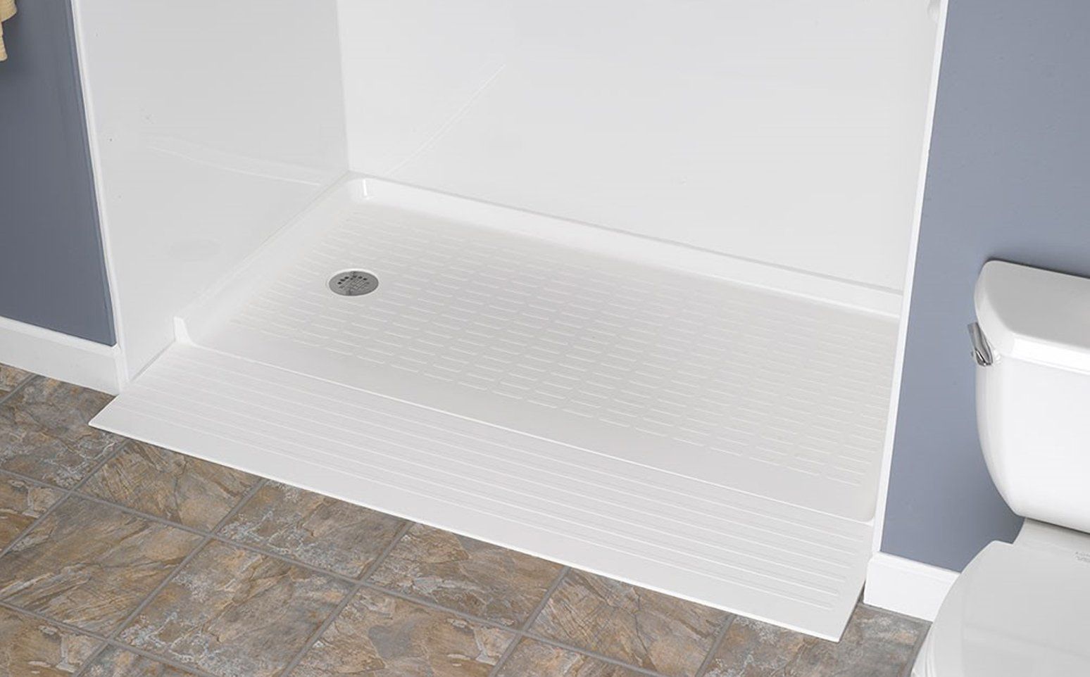 White shower stall with a low threshold, set against a blue wall next to a white toilet, in a bathroom.