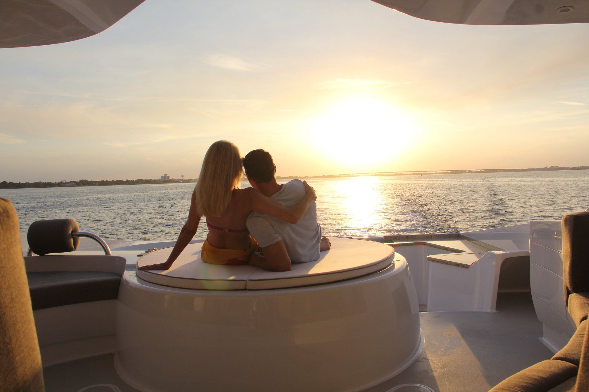 A man and a woman are sitting on a boat looking at the sunset.