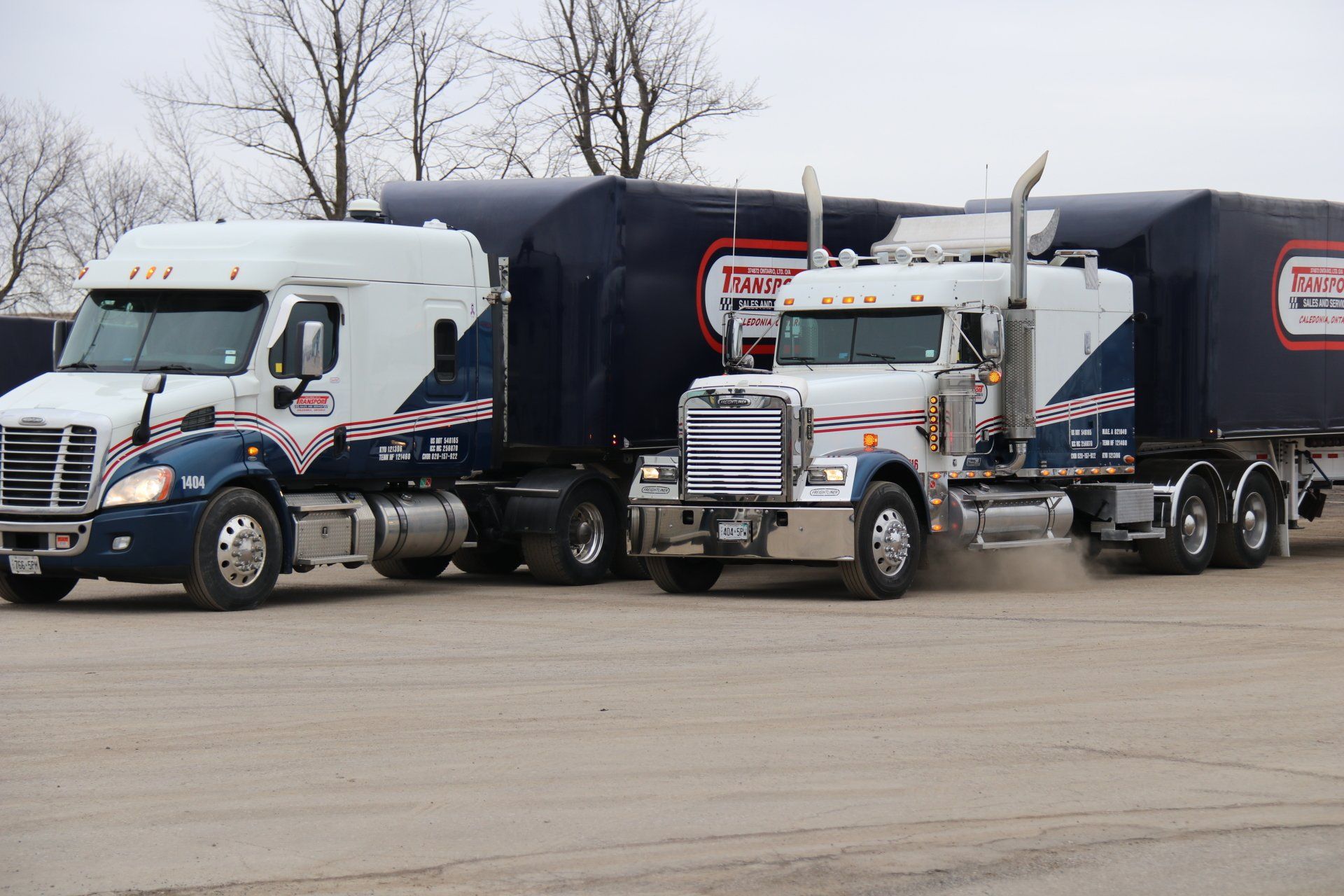 Two semi trucks are parked next to each other on a dirt road