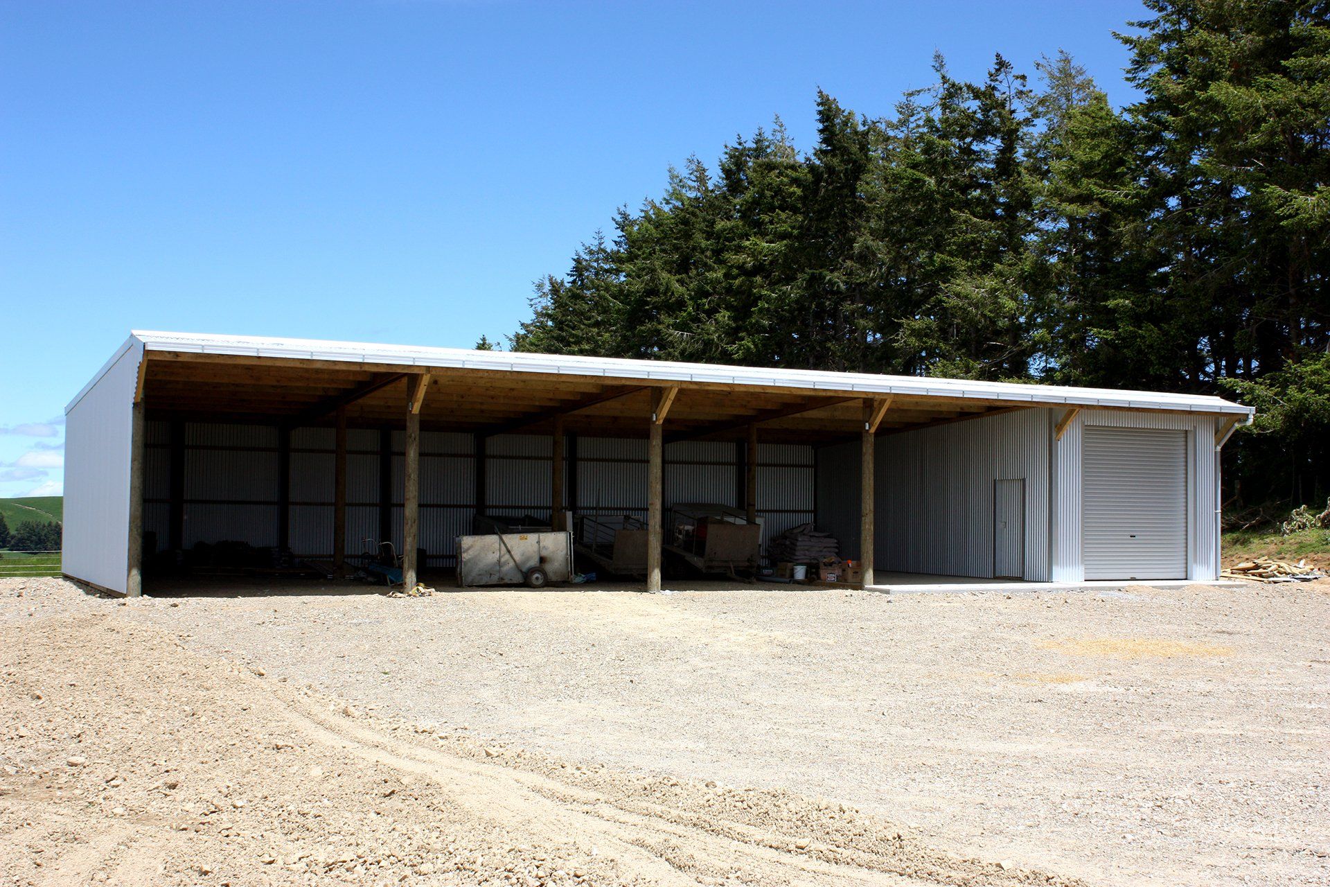 A large, open-sided shed with a gravel floor, wooden support posts, and a closed storage unit on the right.