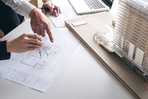Engineering or Creative architect in construction project, Engineers hands working with compasses on construction blueprint building model at a workplace in office, Building and architecture concept.