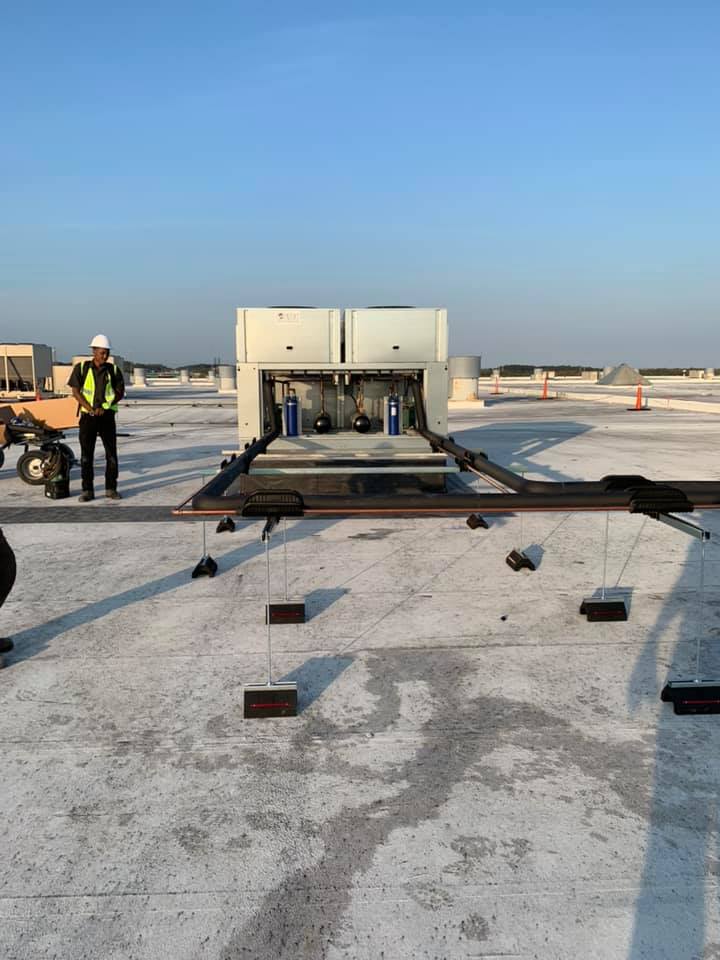HVAC unit on a rooftop with a worker in a vest and hard hat. Blue sky.