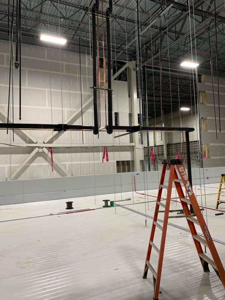Construction site interior with ladder, black pipes, and unfinished walls.