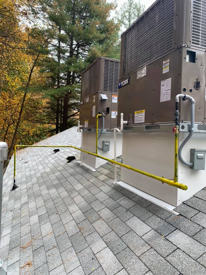 Rooftop HVAC units with yellow safety railings, set against a backdrop of trees and autumn foliage.