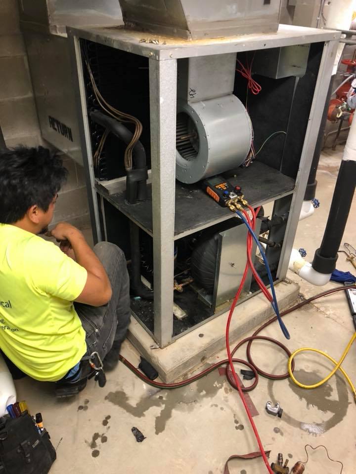 HVAC technician inspecting an air handler unit. The unit is open, revealing