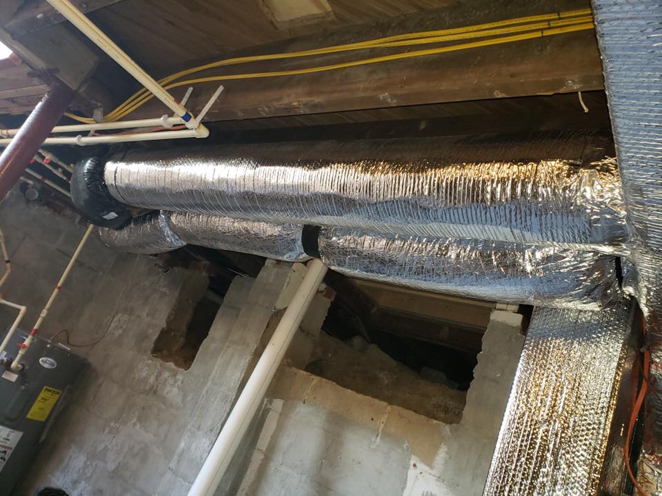 Basement interior with insulated air ducts, pipes, beams, and concrete walls.