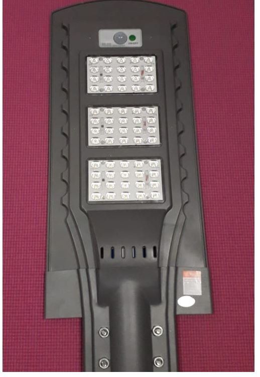 Farola negra alimentada por energía solar con tres paneles LED sobre fondo rojo.