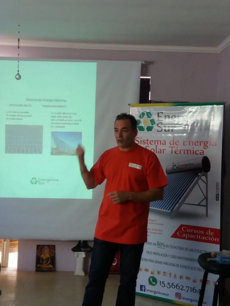 Hombre con camisa roja haciendo una presentación junto a una diapositiva proyectada en una sala de reuniones.