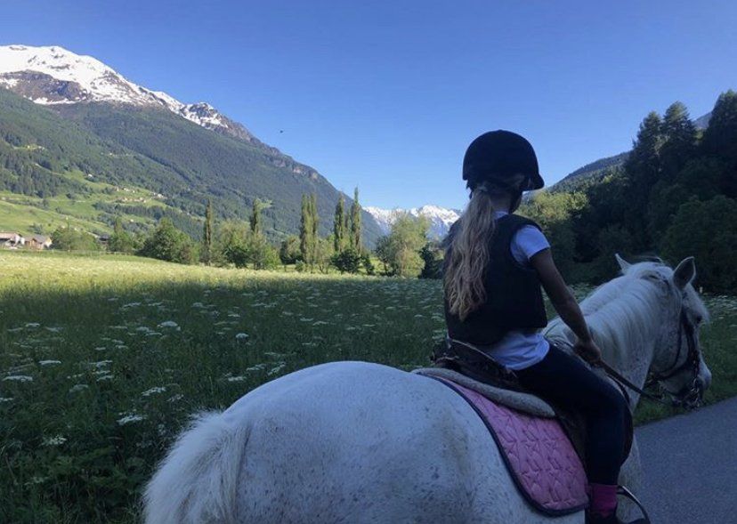 Una ragazza cavalca un cavallo bianco in un campo con le montagne sullo sfondo.
