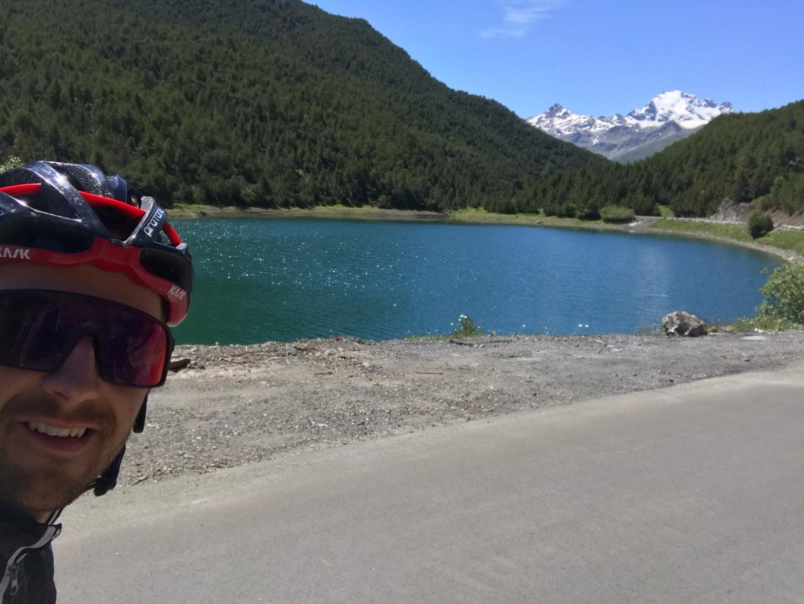Un uomo che indossa un casco e occhiali da sole è in piedi di fronte a un lago