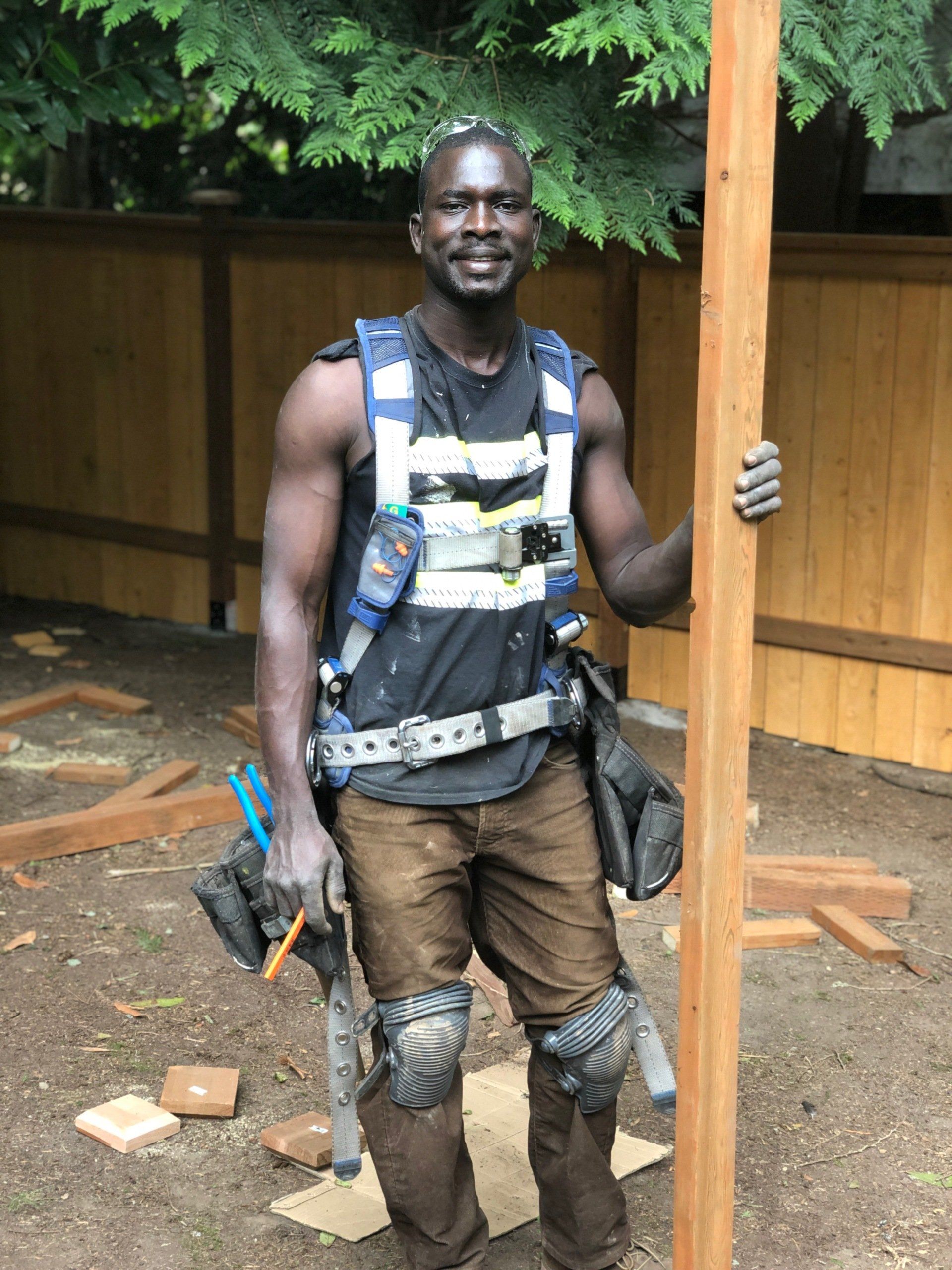 Emmanuel Kidega, owner of Wooden Gate Construction, holding a cedar board on a job site